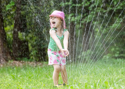 Lapsi pihalla leikkimässä ja vesisuihku suihkuttaa hänen päälle.
