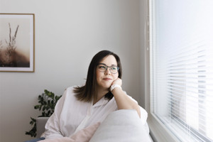 Nuori nainen nauttii uudessa kodissa sohvalla ja katselee mietteliäästi ikkunasta ulos